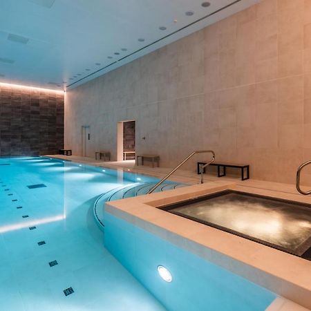 Citysuites 2 Aparthotel Manchester Exterior foto The photo shows an indoor swimming pool area. The pool is a bright blue color and features smooth, tiled surfaces. On one side, there is a hot tub area with steps leading into it. The walls are made of light-colored stone, and there is ambient lighti