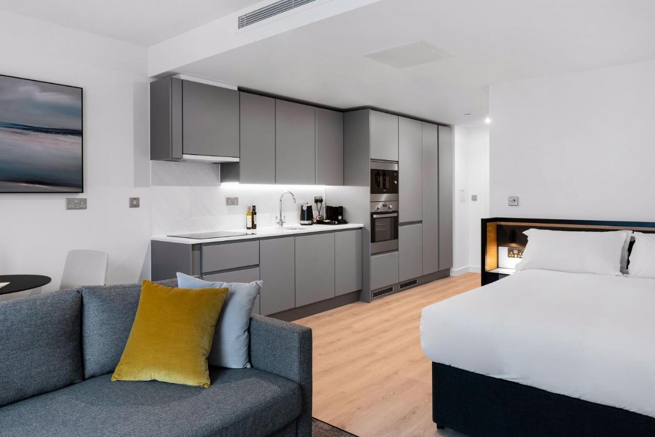 Citysuites 2 Aparthotel Manchester Exterior foto The photo shows a modern studio apartment featuring an open-plan layout. On one side, there is a kitchenette with sleek, gray cabinets and appliances, including a coffee maker and oven. Adjacent to the kitchenette is a small dining area with a table 