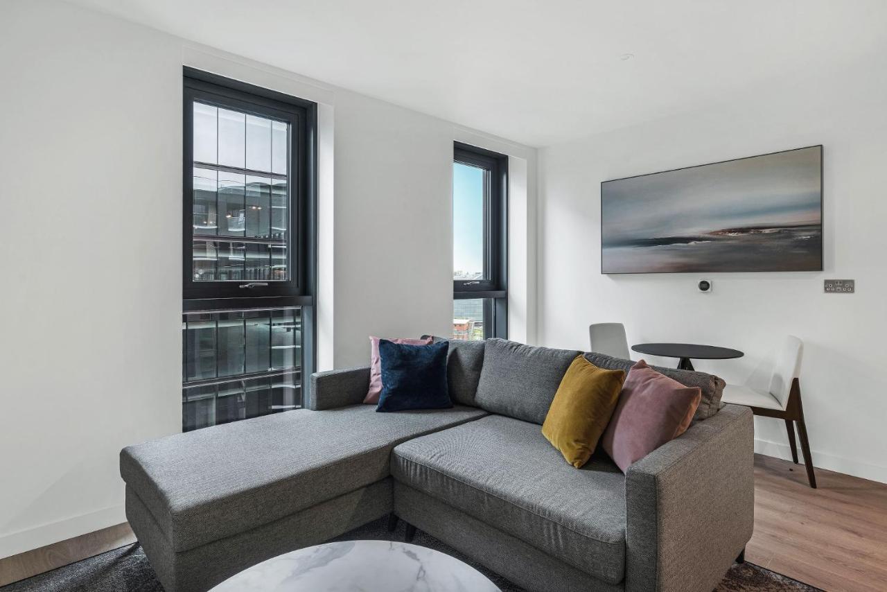 Citysuites 2 Aparthotel Manchester Exterior foto The photo shows a modern living space featuring a gray sectional sofa adorned with colorful throw pillows. There are large windows allowing natural light to fill the room, offering a view of the outdoors. A wall-mounted television is positioned above