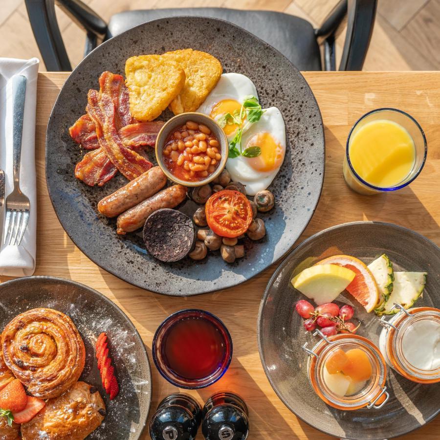 Citysuites 2 Aparthotel Manchester Exterior foto The photo showcases a delicious breakfast spread. On a large, dark plate, there are items including crispy bacon, two fried eggs, baked beans, a grilled tomato, sautéed mushrooms, sausage links, and slices of black pudding. There's also a few pieces 