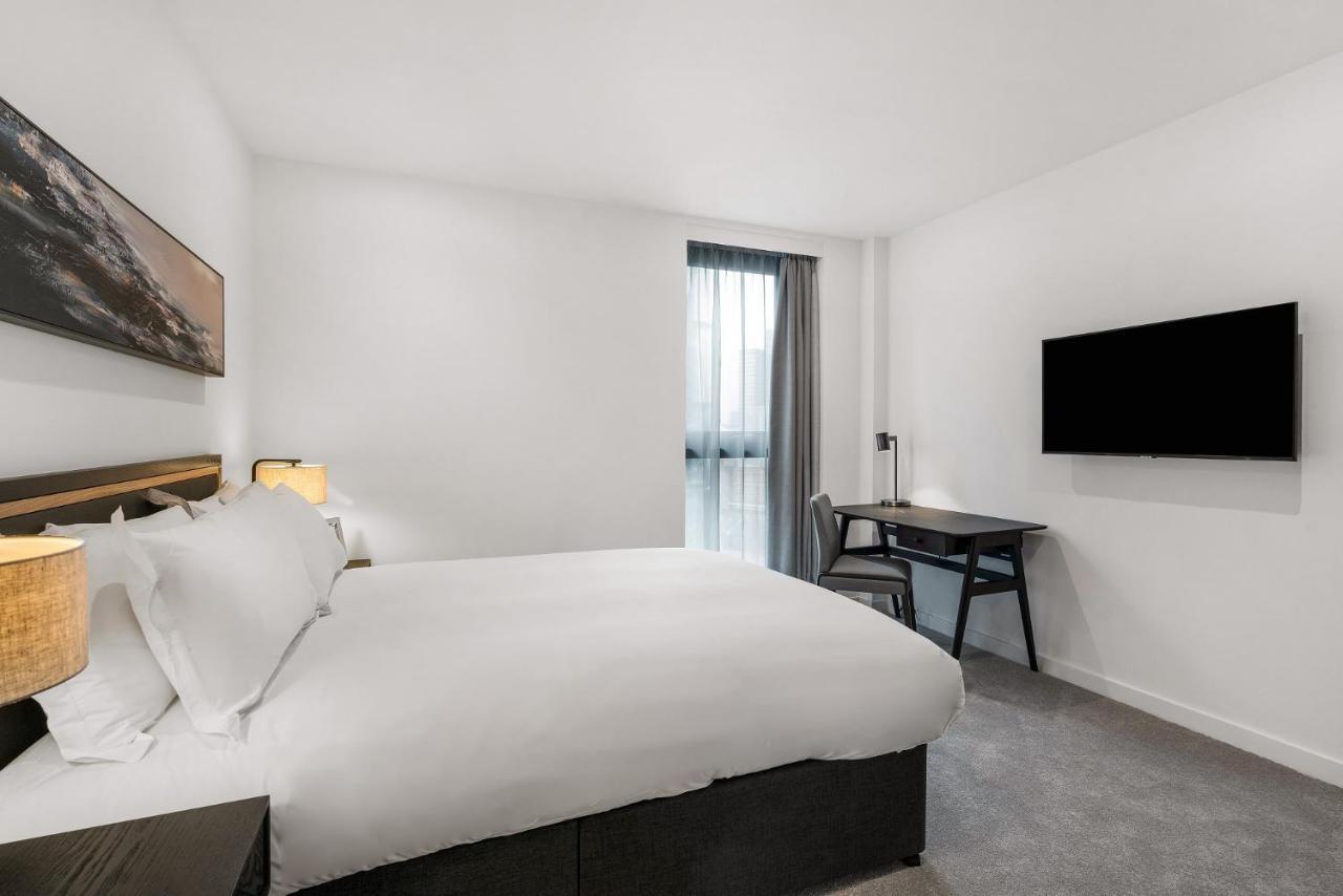 Citysuites 2 Aparthotel Manchester Exterior foto The photo shows a modern hotel room featuring a large bed with white linens and a dark headboard. There are two bedside lamps on either side of the bed. A desk with a chair is placed against one wall, and a flat-screen TV is mounted on another wall. 