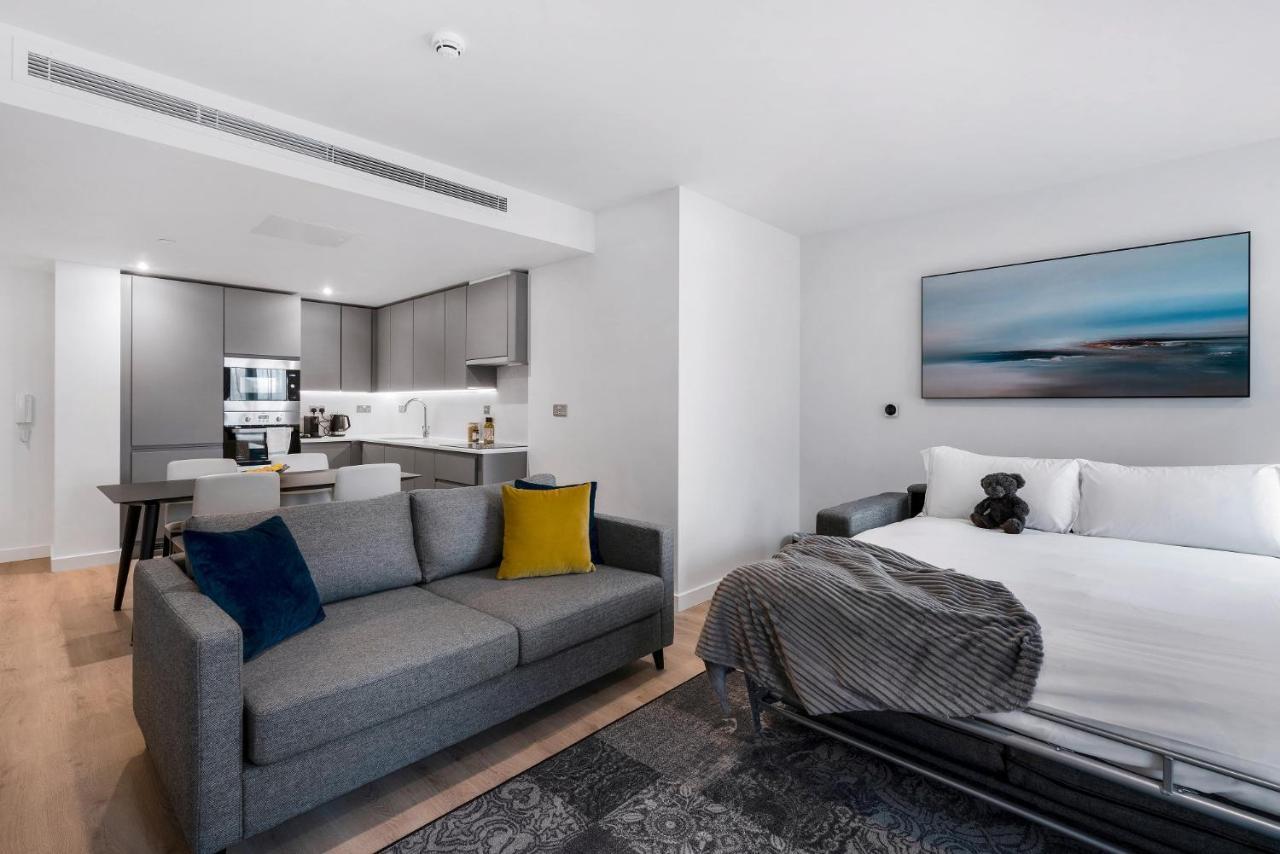 Citysuites 2 Aparthotel Manchester Exterior foto The photo shows a modern, open-concept living space that includes a kitchen and a sleeping area. 

- **Living Area**: On the left, there's a gray sofa with a blue and yellow throw pillow. A blanket is draped over one side, and there's a small dark ru