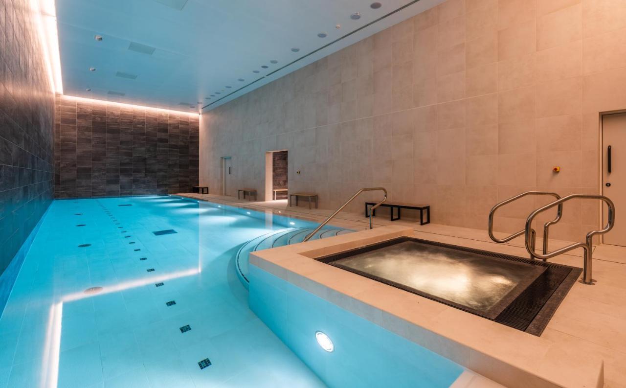Citysuites 2 Aparthotel Manchester Exterior foto The photo shows an indoor swimming pool area. The pool is a bright blue color and features smooth, tiled surfaces. On one side, there is a hot tub area with steps leading into it. The walls are made of light-colored stone, and there is ambient lighti