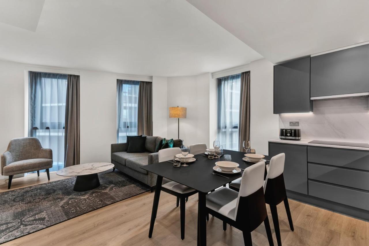 Citysuites 2 Aparthotel Salford  Exterior foto The photo shows a modern living space that includes a dining area and a seating area. There's a sleek black dining table set with plates and cutlery, accompanied by white and black chairs. To one side, a comfortable gray sofa faces the dining area, c