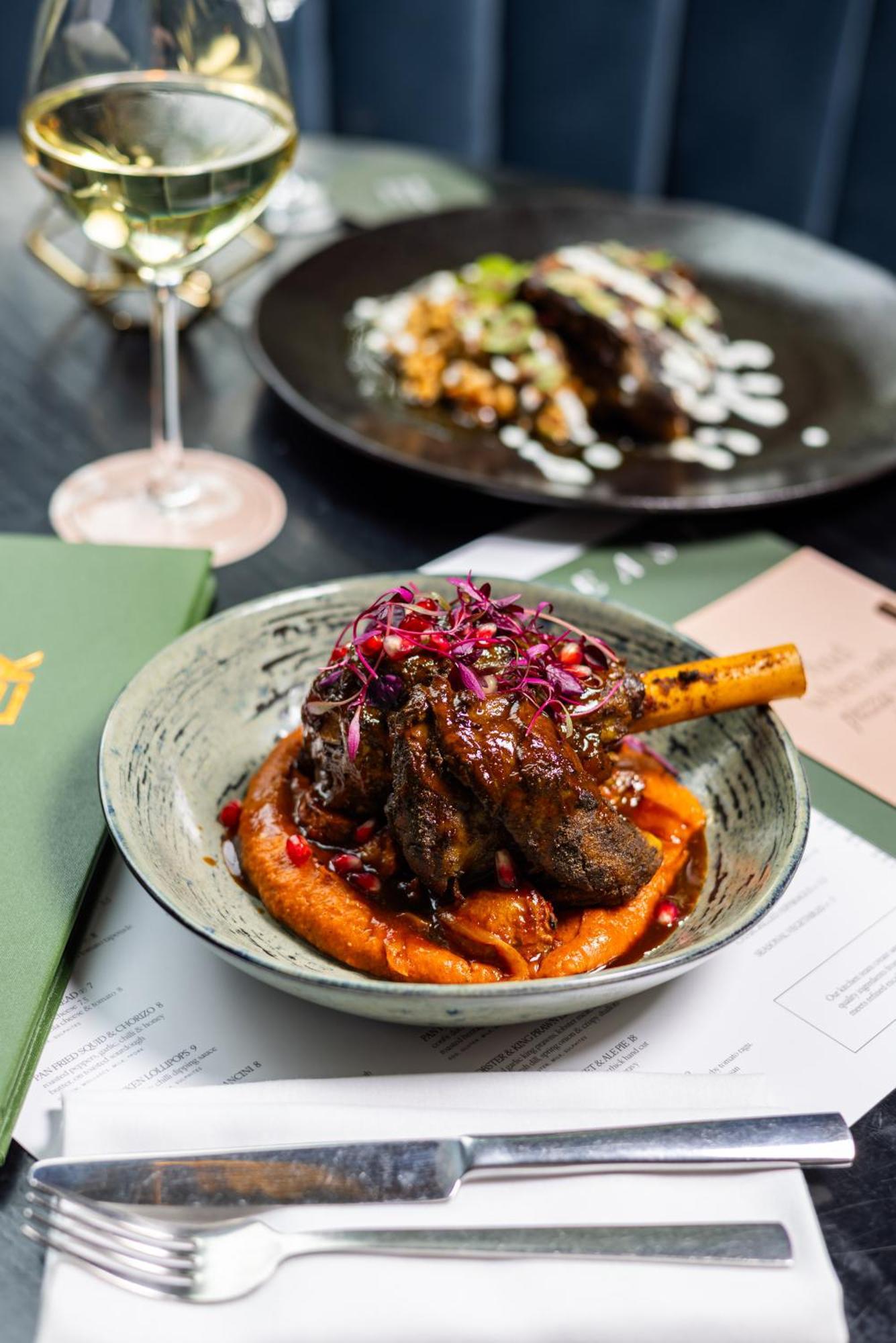 Citysuites 2 Aparthotel Manchester Exterior foto The photo showcases a beautifully presented dish featuring a piece of slow-cooked meat with a bone, likely lamb, sitting atop a vibrant orange puree. The meat is glazed with a rich sauce and garnished with small pieces of red pomegranate and purple m