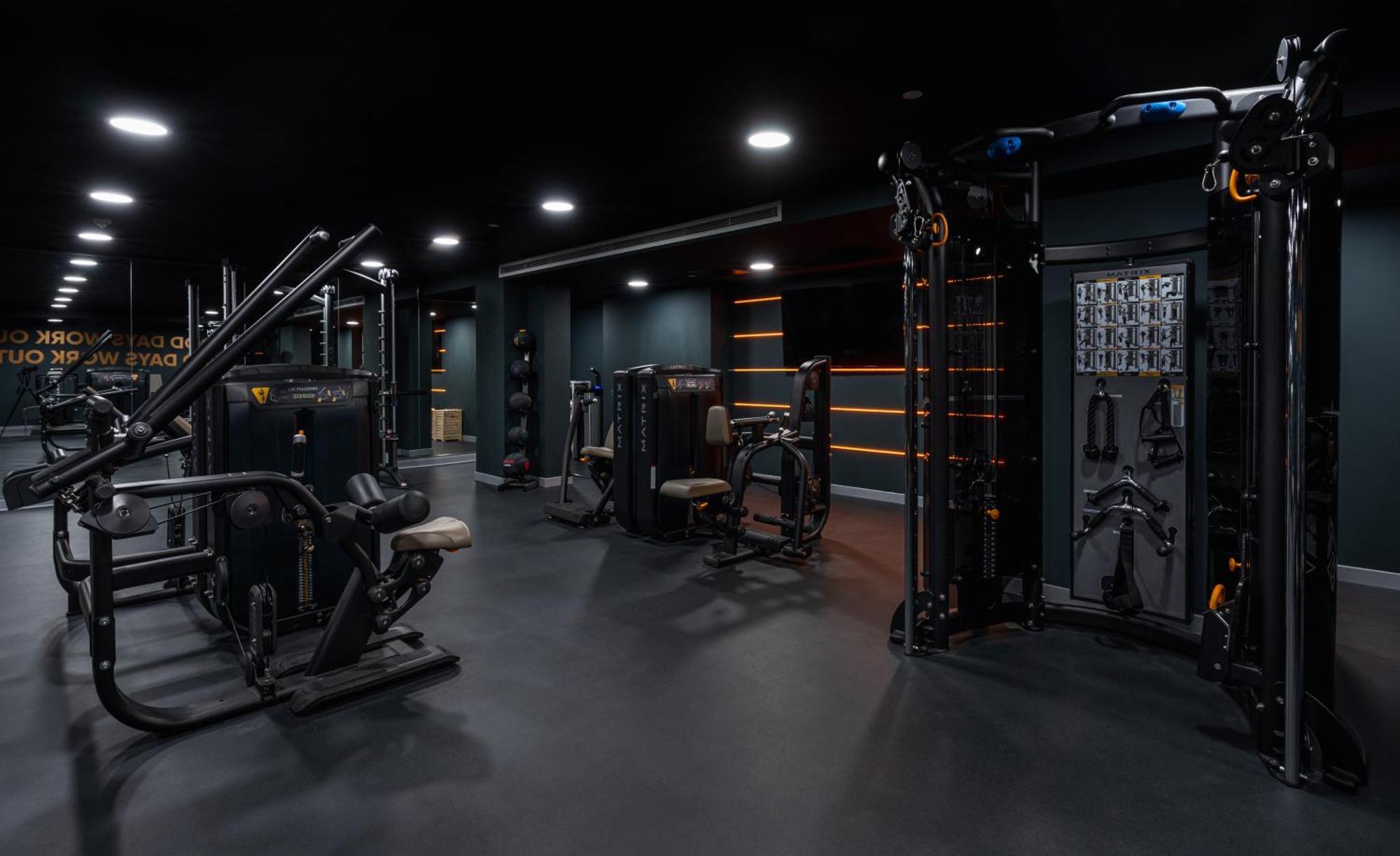 Citysuites 2 Aparthotel Manchester Exterior foto The photo shows a modern gym or fitness area with various workout machines. The space has a dark color scheme, featuring black walls and flooring. There are multiple pieces of exercise equipment, including stations for strength training, possibly tar