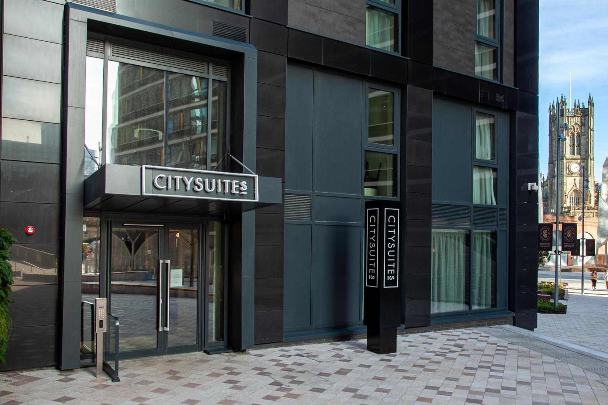 Citysuites 2 Aparthotel Manchester Exterior foto The photo shows the entrance to a modern building labeled "CITYSUITES." The entrance features large glass doors and a sleek, contemporary design. The building has dark exterior panels and large windows, suggesting a stylish and urban environment. The