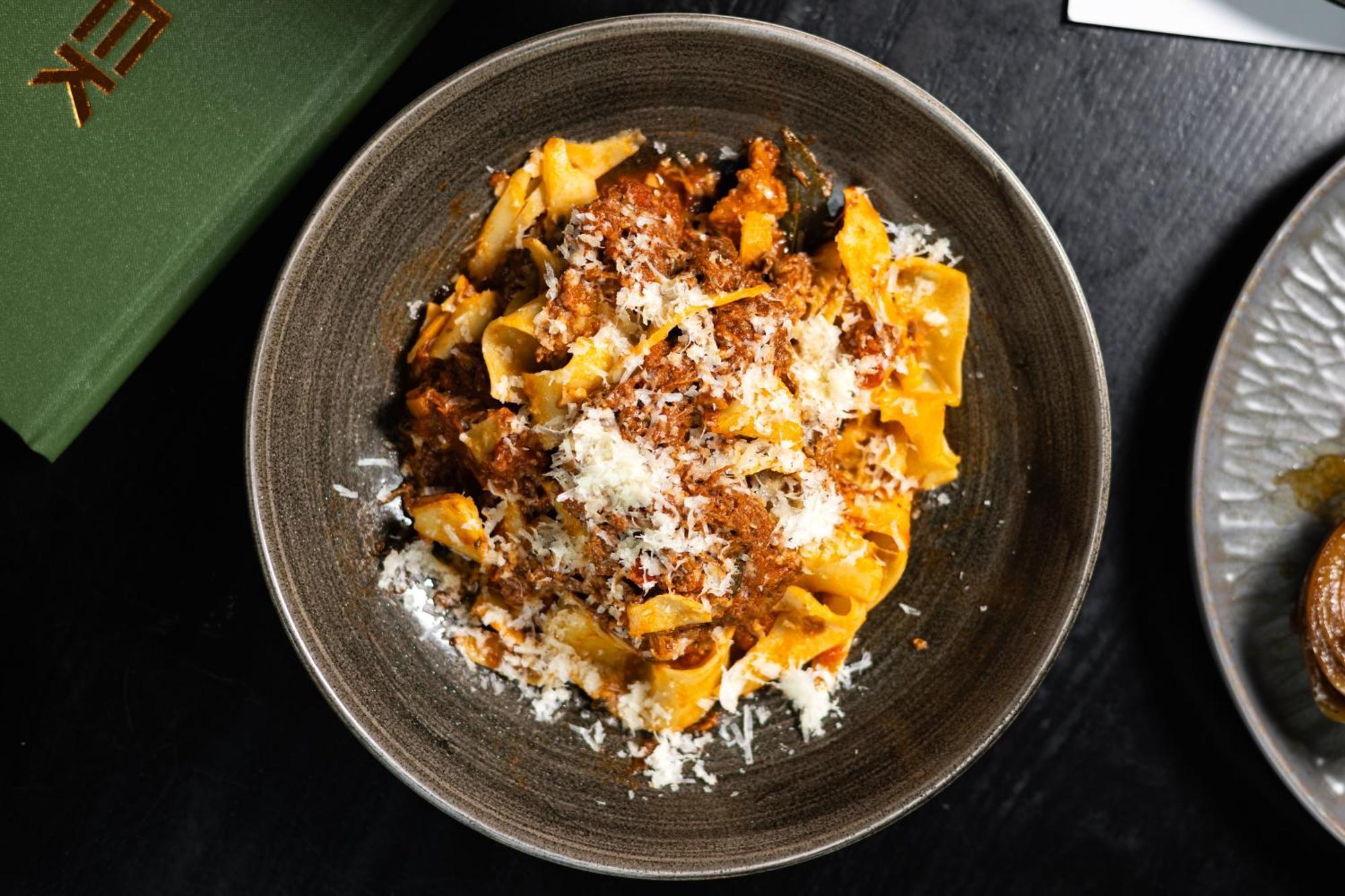 Citysuites 2 Aparthotel Manchester Exterior foto The photo shows a bowl of pasta featuring wide, ribbon-like noodles, likely pappardelle, fully coated in a rich meat sauce. The dish is garnished with a generous sprinkling of grated cheese, adding a creamy texture to the presentation. The dark bowl 